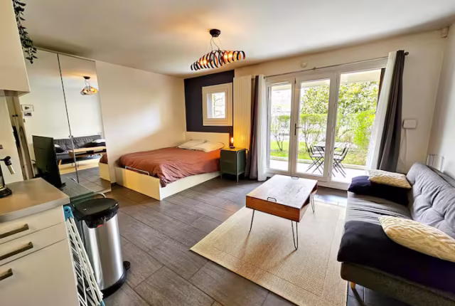 studio moderne bien agencé, où l’on peut voir un coin salon et un coin chambre délimités par un joli tapis, des meubles multifonctionnels comme un canapé-lit ou une table extensible