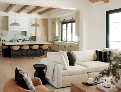 Une pièce à vivre baignée de lumière naturelle : murs blancs cassés, fauteuil en lin beige accessible (accoudoirs larges, hauteur adaptée), plante verte dans un pot en terre cuite artisanale, table basse en bois recyclé.
