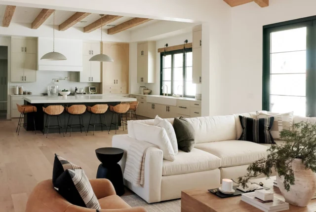 Une pièce à vivre baignée de lumière naturelle : murs blancs cassés, fauteuil en lin beige accessible (accoudoirs larges, hauteur adaptée), plante verte dans un pot en terre cuite artisanale, table basse en bois recyclé.