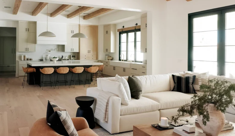 Une pièce à vivre baignée de lumière naturelle : murs blancs cassés, fauteuil en lin beige accessible (accoudoirs larges, hauteur adaptée), plante verte dans un pot en terre cuite artisanale, table basse en bois recyclé.