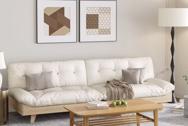 Un salon baigné de lumière naturelle, canapé en lin beige avec coussins doux, plaid en laine, table basse ronde en bois clair, lampe sur pied minimaliste, tapis structuré, et une plante haute dans un pot blanc mat.